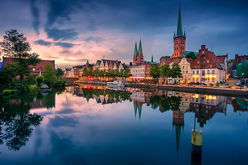 Cityscape of riverside Lübeck with reflection of the city in the Trave River at sunset, Germany. Via Shutterstock / Rudy Balasco.