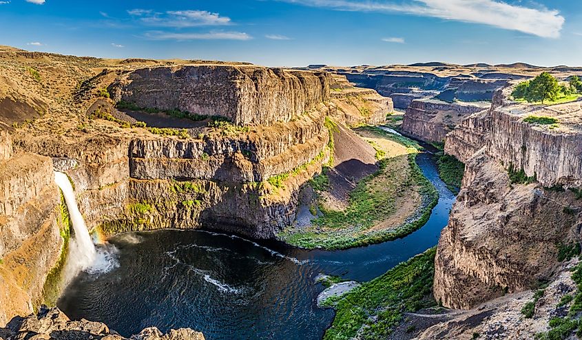 The Palouse Falls in Washington, US emptying into a gorge with a rainbow in the falls and blue skies