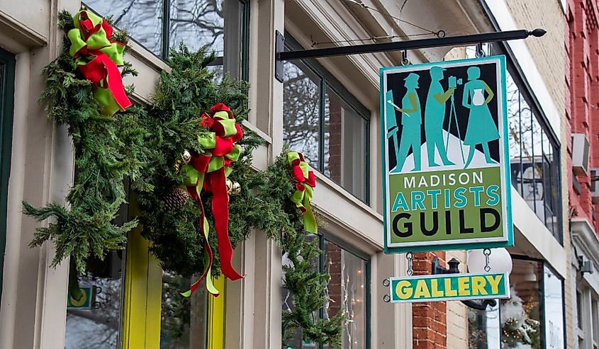 Festive gallery storefront with a "Madison Artists Guild" sign. Green garland and red bows adorn the entrance, creating a cheerful holiday atmosphere.