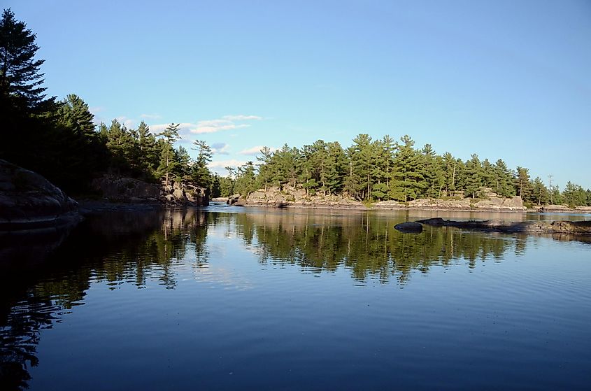 Symmetrical reflections of the sky, trees, and Canadian shield rock islands in the surface of a river