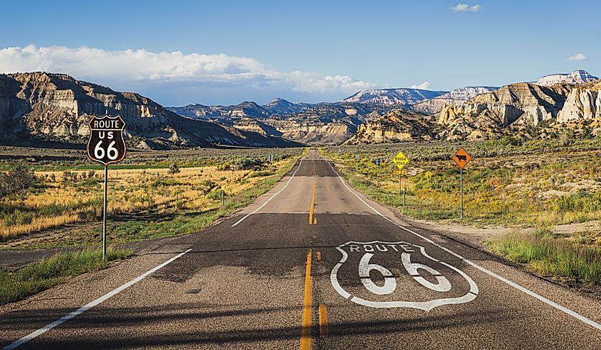 Scenic panoramic view of long straight road on famous Route 66 with historical street signs and paintings in classic american wild western mountain scenery in beautiful golden evening light at sunset