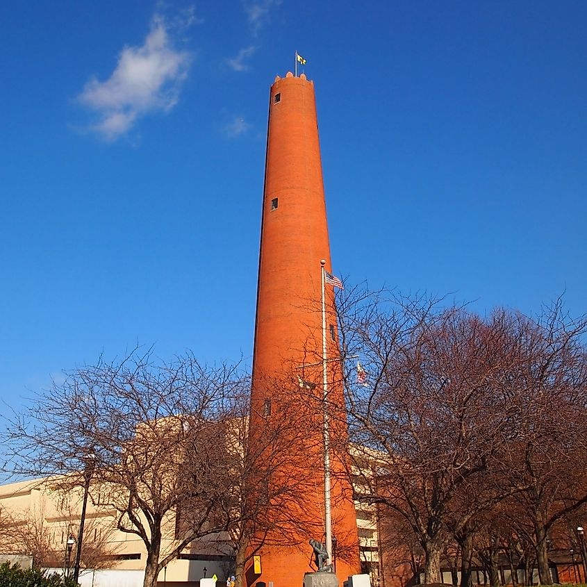 The historic Phoenix Shot Tower, in Baltimore, MD, seen on a clear, winter day with bare trees and a blue sky.