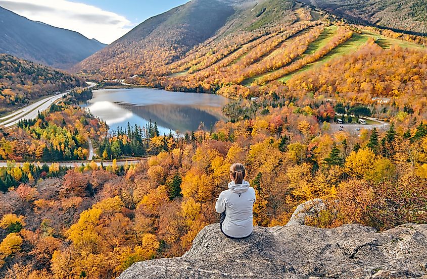Woman hiking at Artist's Bluff in autumn with a view of Echo Lake and fall colors in Franconia Notch State Park, White Mountain National Forest, New Hampshire, USA.