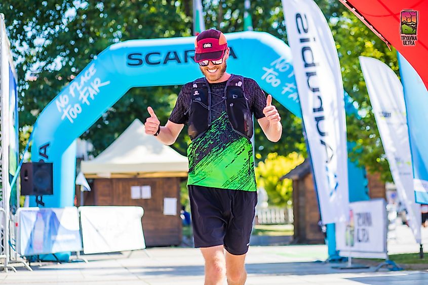 A runner crossing the finish line, flashing two thumbs up to the camera.