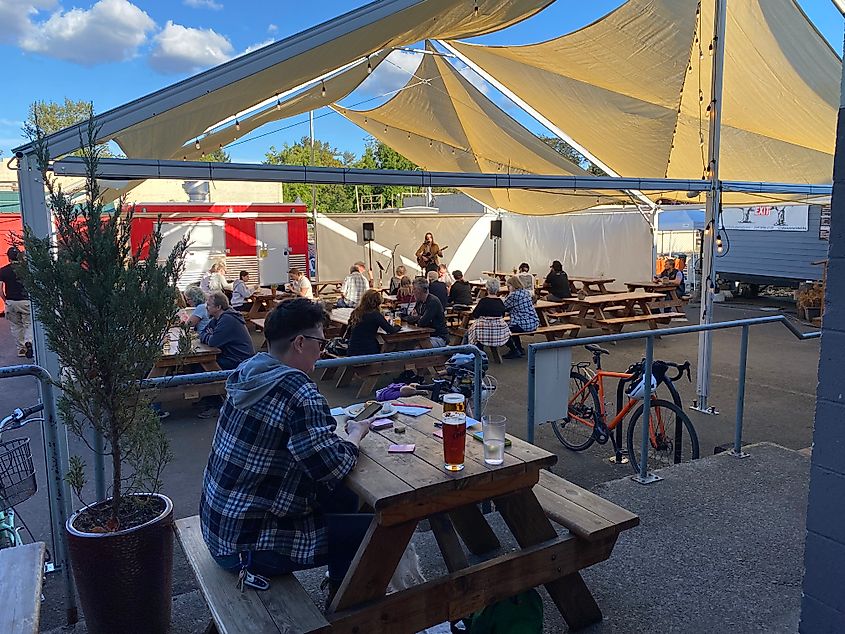 A crowd enjoying pints at picnic tables underneath an event tent while listening to live music.