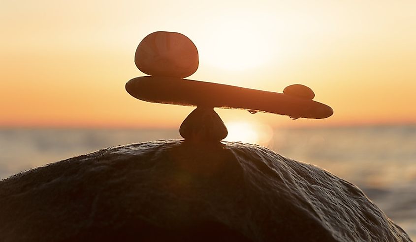 Imbalance of forces - natural scales of stones ( in imbalance) at the sea to the orange sunset 