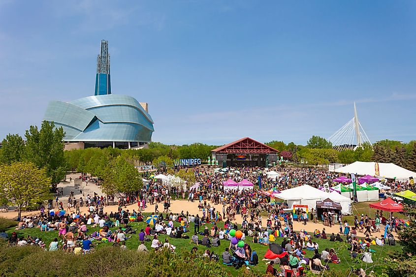 A large assembly of people is gathered at The Forks to celebrate Pride Weekend in Winnipeg, Canada