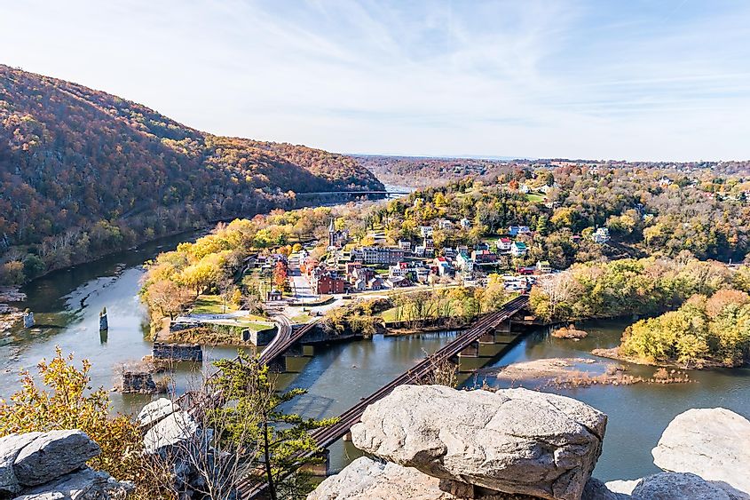 Harper's Ferry overlook closeup of cityscape with cliffs rocks, colorful orange yellow foliage fall autumn forest with small village town by river in West Virginia