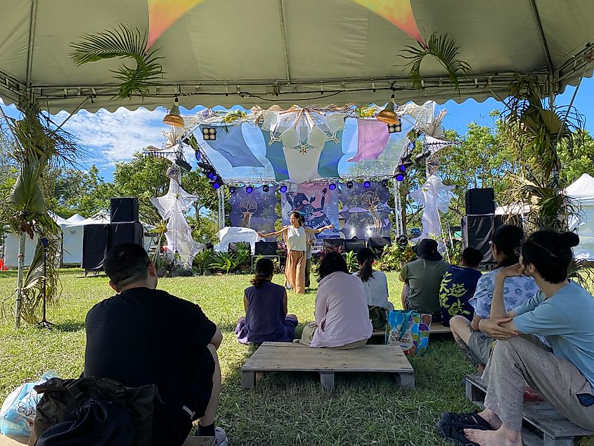 A small audience watches a group of dancers at an outdoor hippie festival.