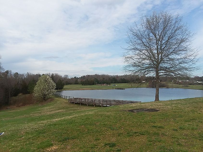 Pond at Paul C. Edmunds Park with trees and cloudy blue sky.