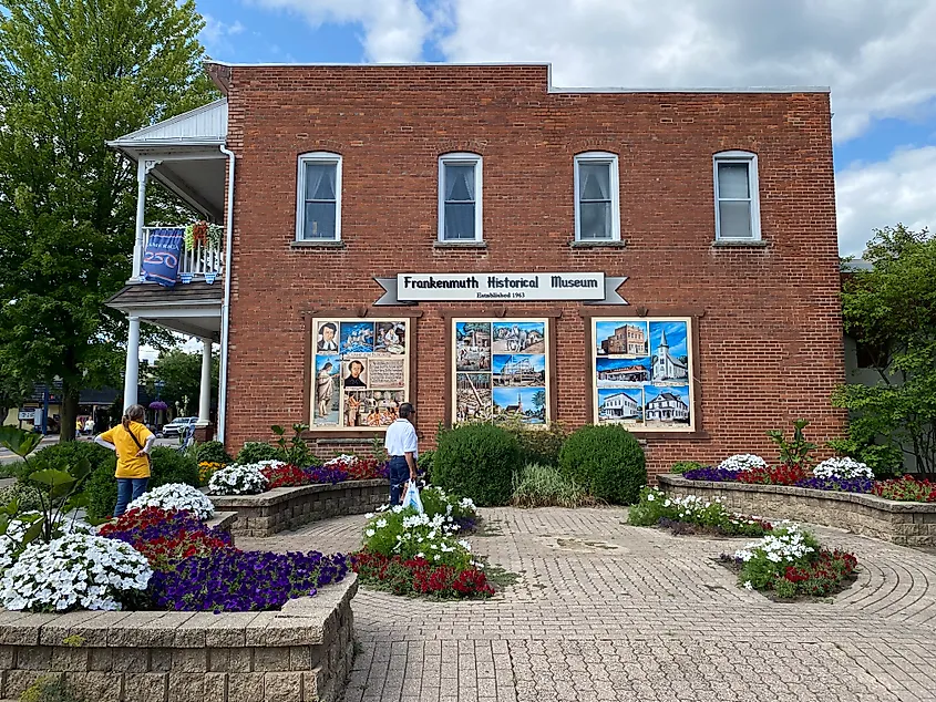 A couple investigates the brick wall mural and surrounding flower garden of the Frankenmuth History Museum