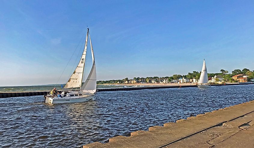 Two sailboats traveling up the black river from Lake Michigan towards the harbor in South Haven, Michigan, USA with blue sky copy space.