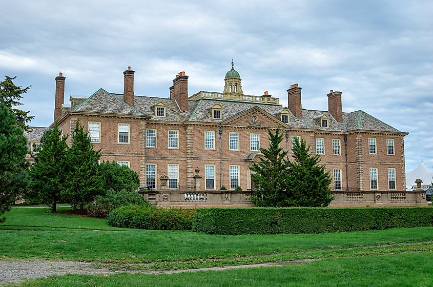 Large historic brick mansion in Ipswich, Massachusetts, with multiple chimneys, a central cupola, and manicured lawns and hedges in the foreground.