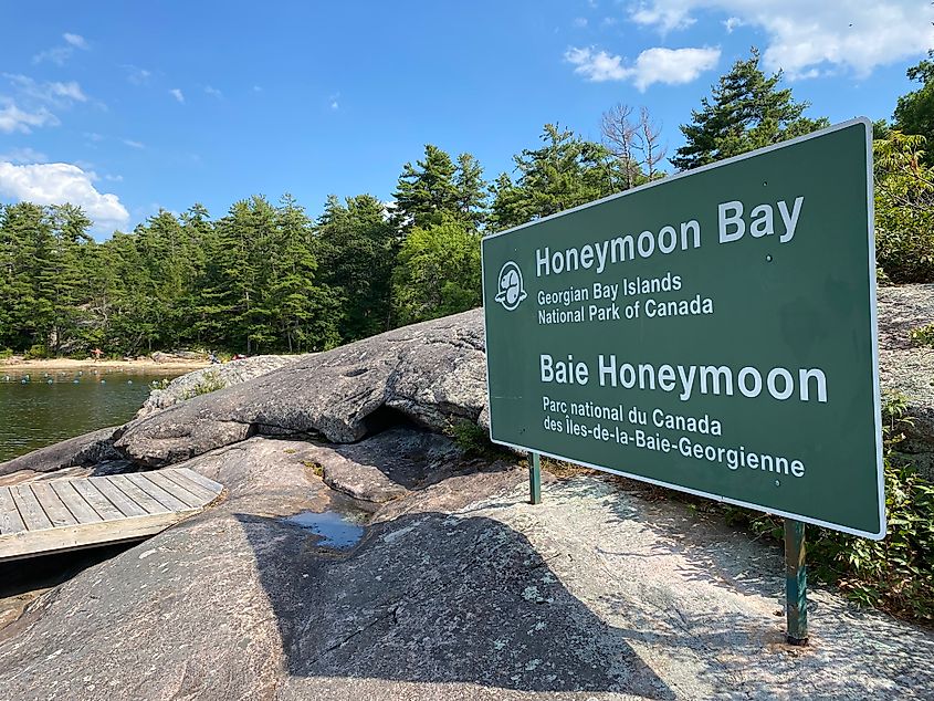 A green Georgian Bay Islands National Park sign stands on the granite rocks indicating Honeymoon Harbour.