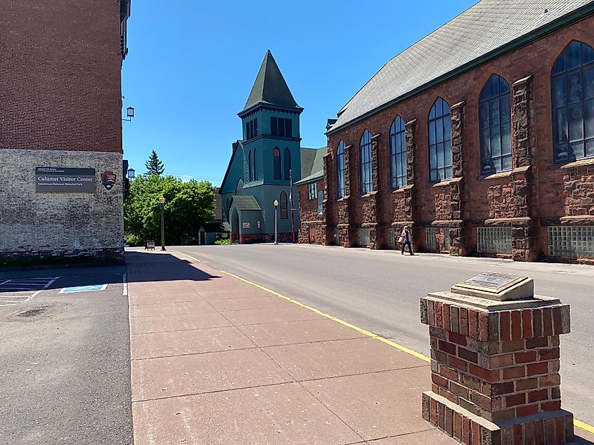Large, red-brick buildings sandwich a blue steeple. 