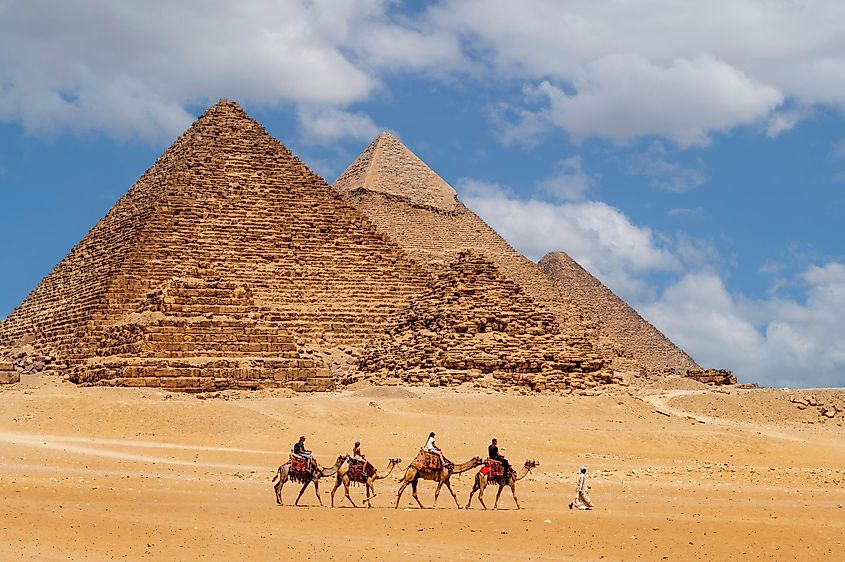 Group of tourists riding camels in the Giza pyramid complex. 