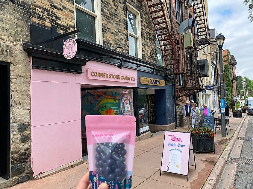 Holding up a bag of blueberry chocolates outside of the pink colored Corner Store Candy Co