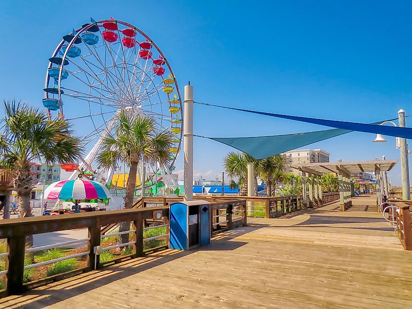 A large, colorful Ferris wheel at the Carolina Beach boardwalk in North Carolina under a blue sky.