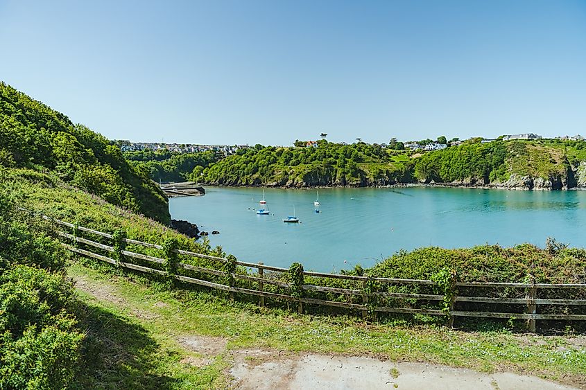 Scenic coastal walking path with wooden fence overlooking harbor waters in Fishguard Lower Town, Pembrokeshire, Wales.