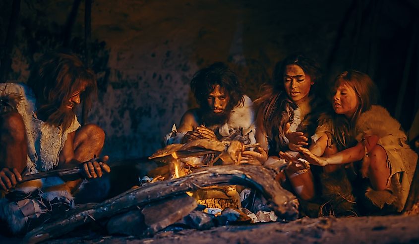 Tribe of Prehistoric Hunter-Gatherers Wearing Animal Skins Grilling and Eating Meat in Cave at Night