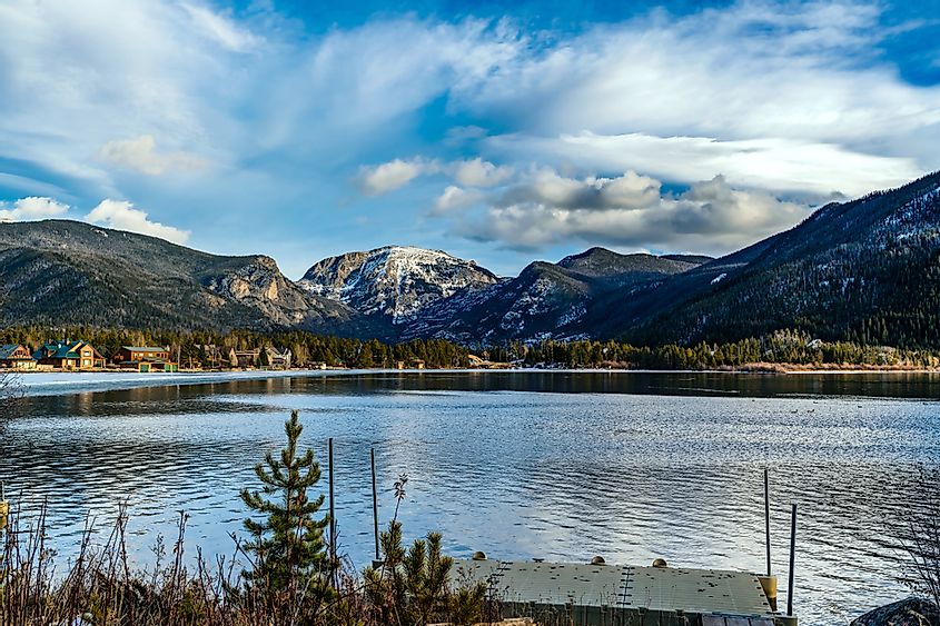 Views of the Rocky Mountains snow covered mountain tops from across a still smooth lake with majestic clouds overhead in Grand Lake, Colorado
