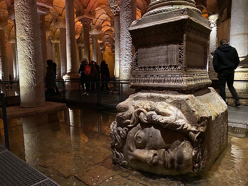A pillar with a sideways Medusa head stands in a small pool of water, within a large underground cistern.