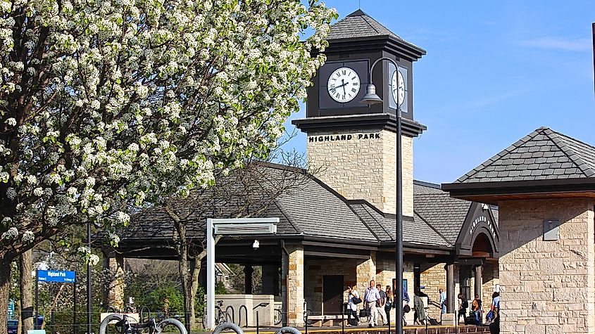 A springtime late afternoon view of the Metra station in Highland Park, with commuters after the train had left, a clock tower and spring white tree blossoms.