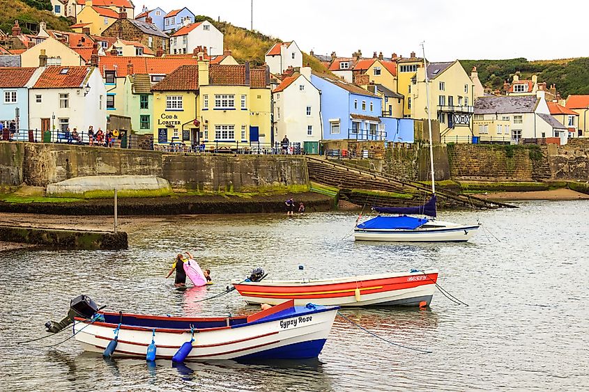 Small boats moored in Staithes Harbour with children playing along the shore in North Yorkshire, England
