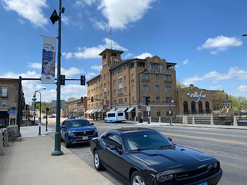 Cars parked on a walkable main street in front of the historic, beige-brick Hotel Baker.