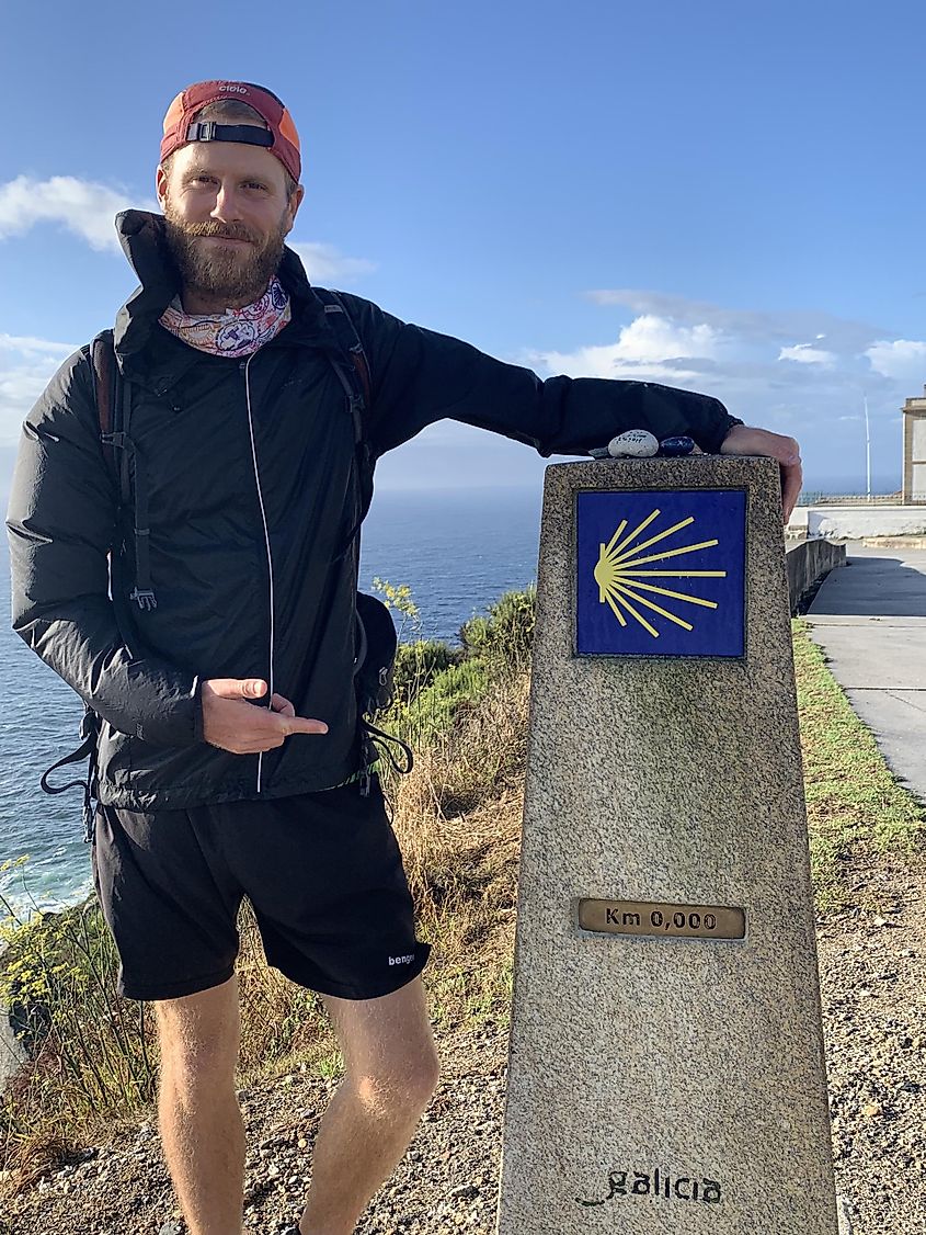 A male hiker poses next to a 0km distance marker on the Camino de Santiago.