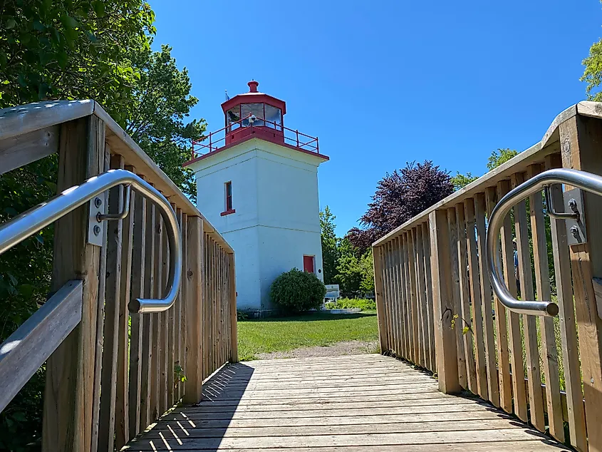 A small white and red lighthouse as seen approaching the top of a wooden staircase. 