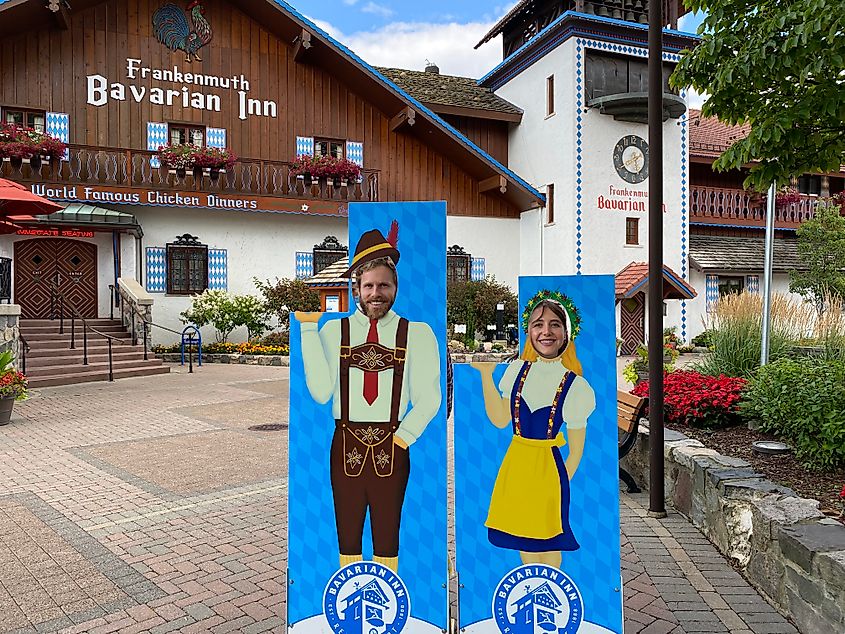 A couple poses in one of those face-in-hole attractions, depicting them in traditional Bavarian attire.
