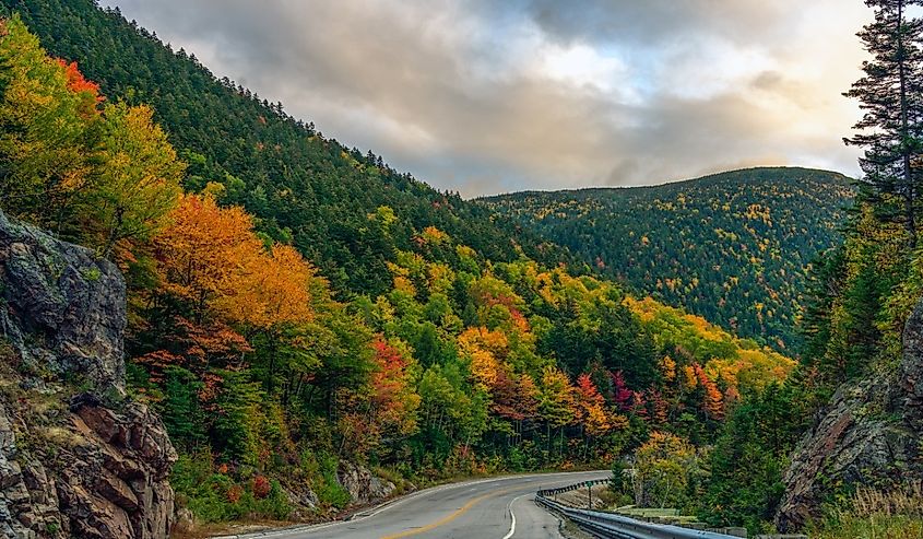 A two-lane highway winds through colorful autumn foliage at Crawford's Notch in New Hampshire's White Mountains.