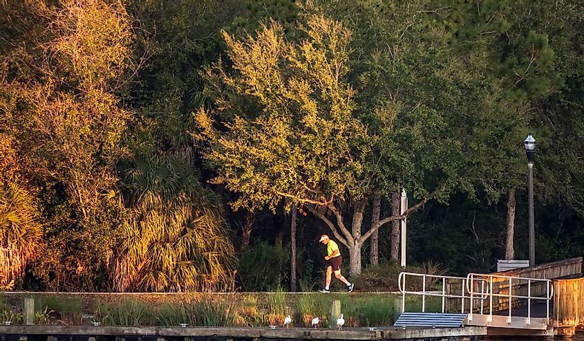 A senior man jogs along a lakeside path in the light of the rising sun in Lakewood Ranch, Florida