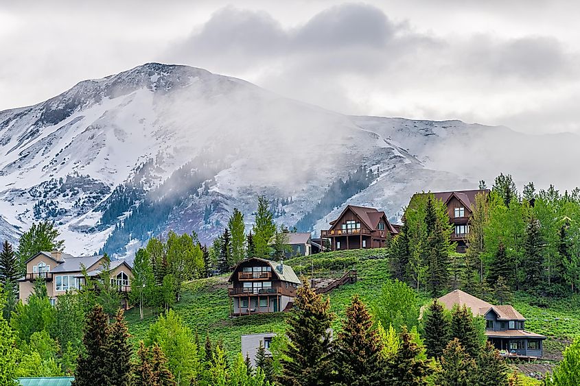 Crested Butte, USA, Colorado town village in summer with clouds and foggy mist morning and houses on the hillside with green trees.