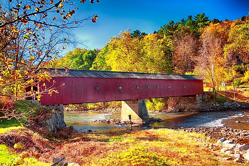 Fall colors envelop the iconic West Cornwall Covered Bridge spanning the Houstanic River in Connecticut.