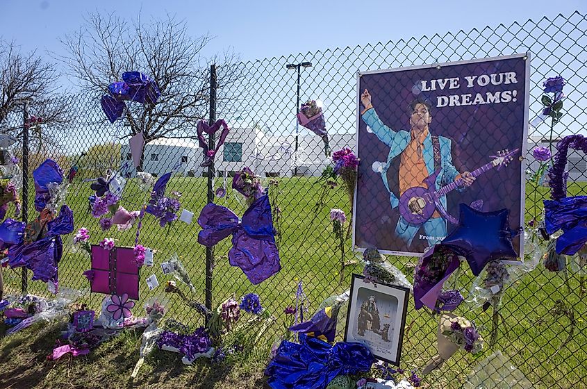 Prince's Live Your Dreams! poster on memorial fence playing Love Symbol guitar at Paisley Park Studios.