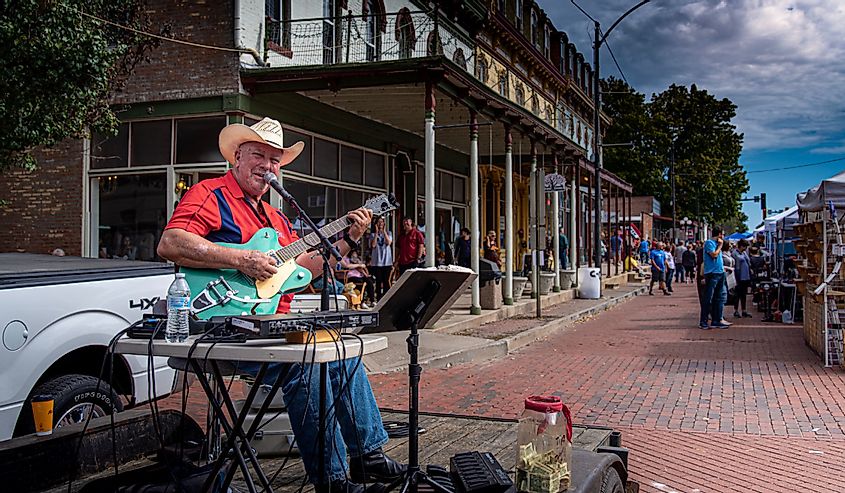 Country folk singer on stage street performing with guitar on red brick road during fall festival with old buildings and craft booths in background in Lebanon 