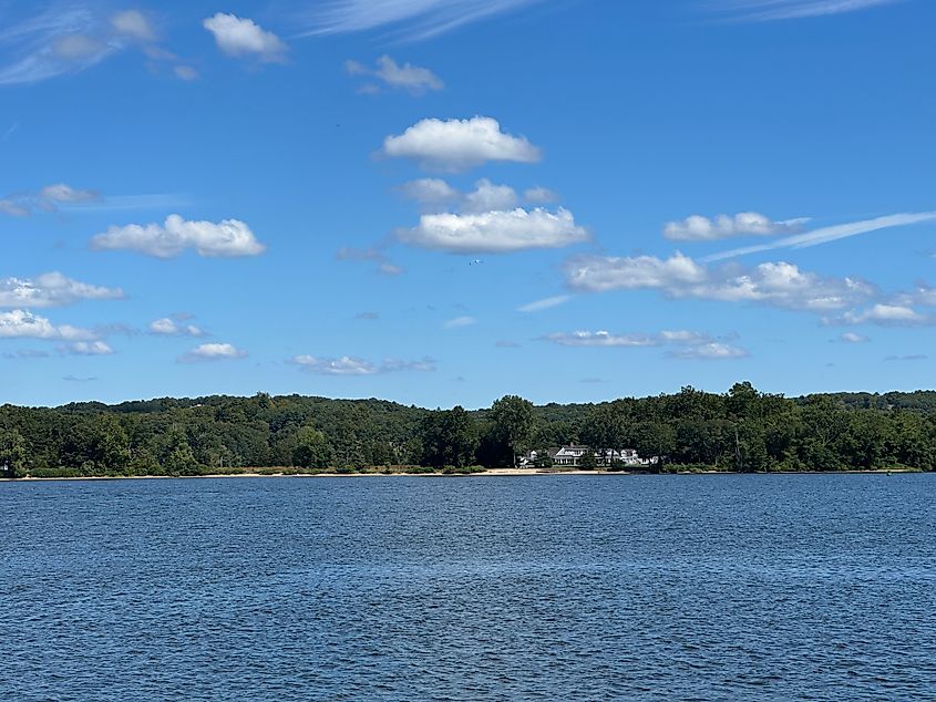 View across the Connecticut River from Chester, Connecticut showing calm water, a wooded shoreline, and a few houses beneath a sky with scattered clouds.