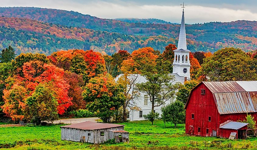 Red barn and church next to a harvested cornfiield with the Autumn colors in the background, Woodstock, Vermont