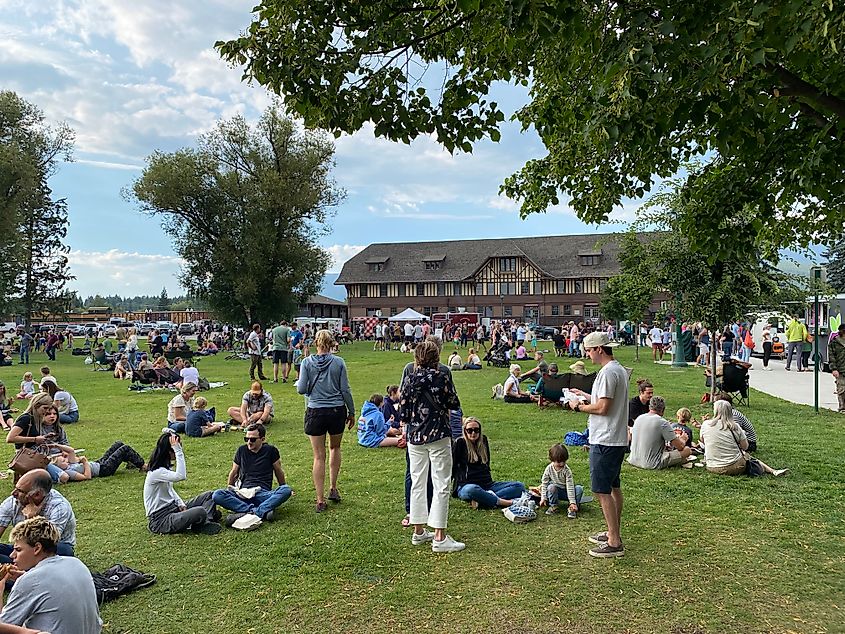 A summer crowd gathers in a park outside of a train depot. 