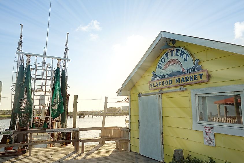 Editorial Photo Credit: zimmytws via Shutterstock. SOUTHPORT,NC - USA - 06-29-2021: Potters Seafood Market and fishing boat on the Cape Fear River in Southport