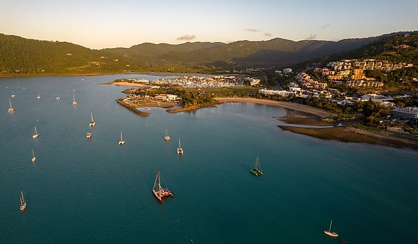 Aerial View overlooking a coastal town with multiple boats anchored in calm, turquoise waters at sunset in Airlie Beach, Australia.
