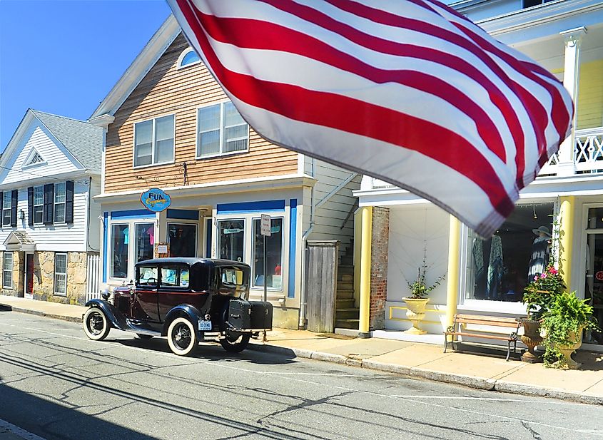 Stonington, Connecticut: American flag blowing in the wind with a vintage car in the background in a small New England town.