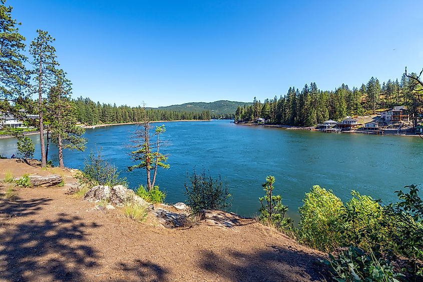 The Spokane River in Post Falls, Idaho, with waterfront homes along the shore near Black Bay Park on a summer day.