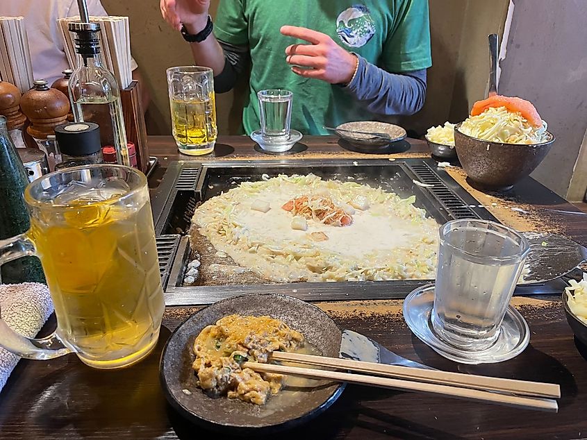 A restaurant table with a stovetop on it, cooking the Japanese specialty, monjayaki (savory pancake)