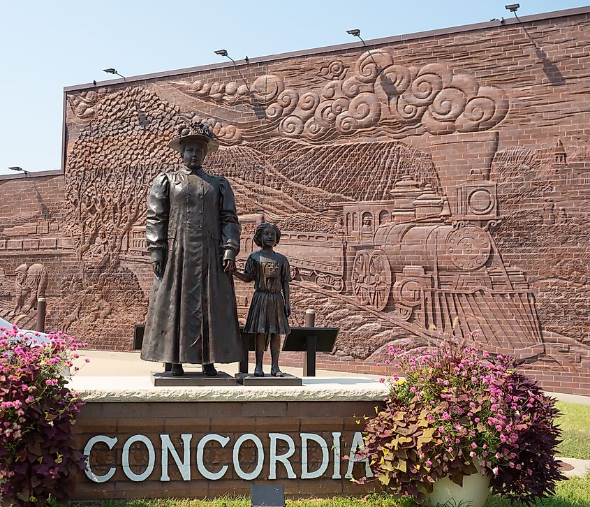 Statue of orphan placement agent Anna Laura Hill standing with an orphan train rider against the backdrop of the whole wall mural in Concordia, Kansas.