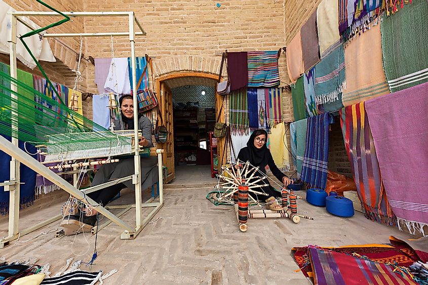 Woman weaves fabric with traditional way and another woman spins the wool in Meybod, Iran.
