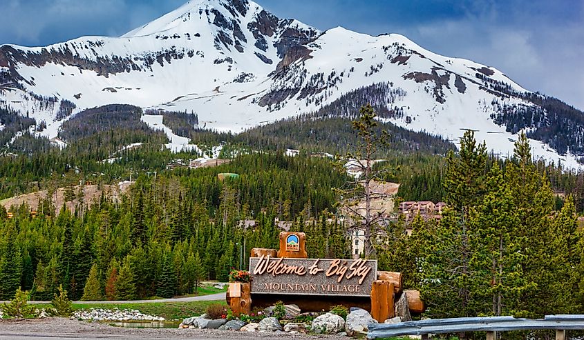 Welcome to Big Sky Mountain Village Signage, dwarfed by the enormity of Lone Mountain full of snow in the Madison Range in the state of Montana