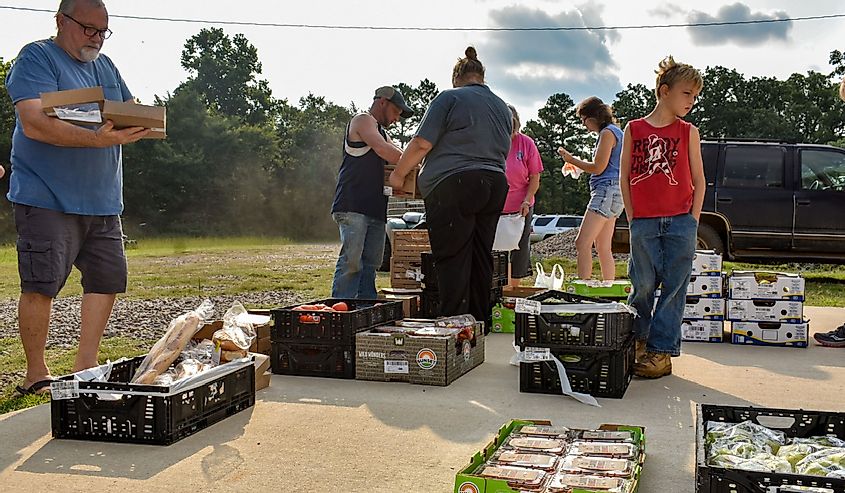 Free groceries being given away to the needy at a small local fire department, a group of people gathering up food to take home and eat, Black Fork, Arkansas.